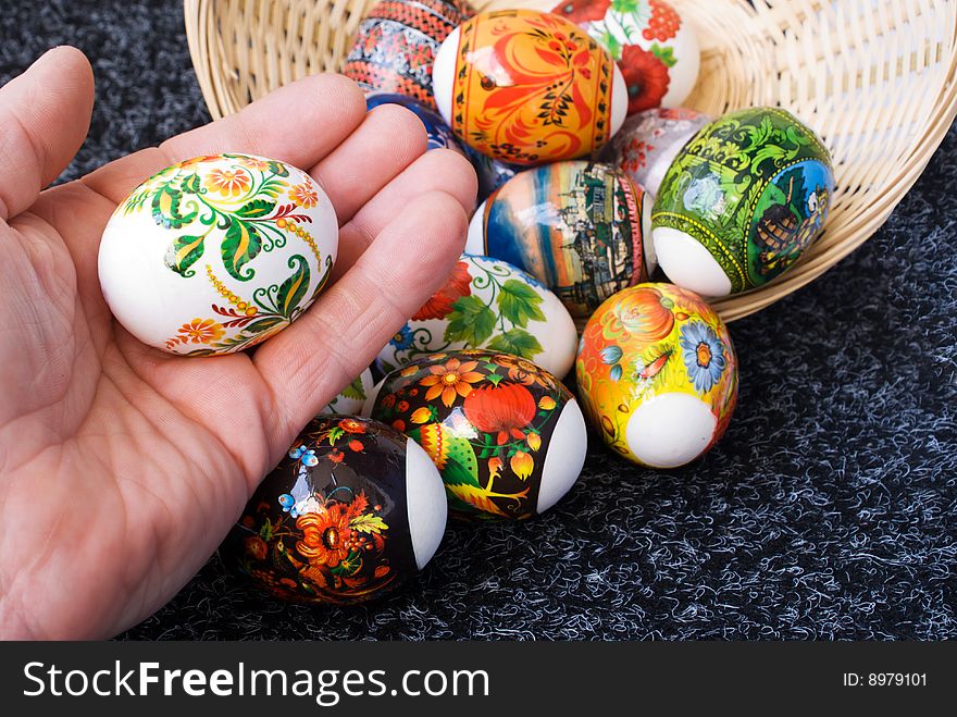 A hand lays an easter egg in a small basket. A hand lays an easter egg in a small basket