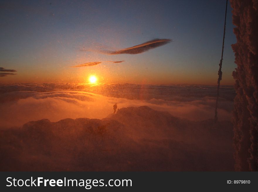 A person alone above the clouds in windy conditions with blowing snow