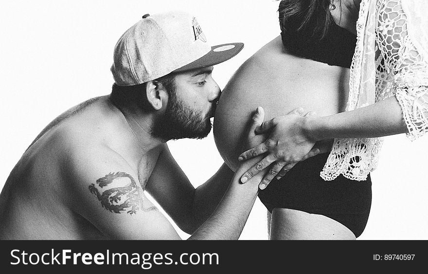 A black and white image of a man kissing the pregnant woman's belly. A black and white image of a man kissing the pregnant woman's belly.