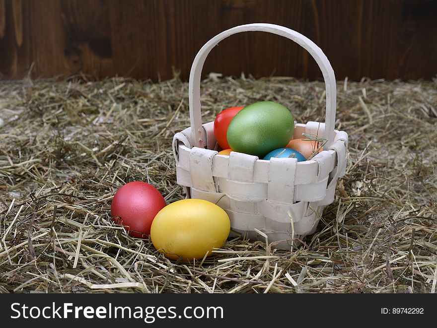 Colorful dyed Easter eggs in white wicker basket in straw of rustic barn. Colorful dyed Easter eggs in white wicker basket in straw of rustic barn.
