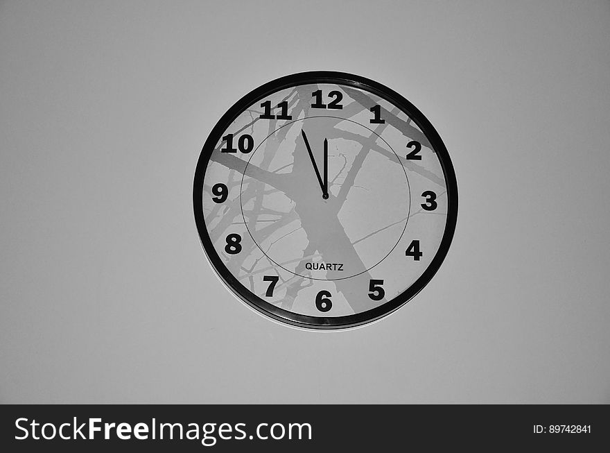 Quartz clock on pale gray wall showing five (four) minutes to midnight, ghostly reflections in the glass, concept of time to doomsday. . Quartz clock on pale gray wall showing five (four) minutes to midnight, ghostly reflections in the glass, concept of time to doomsday. .