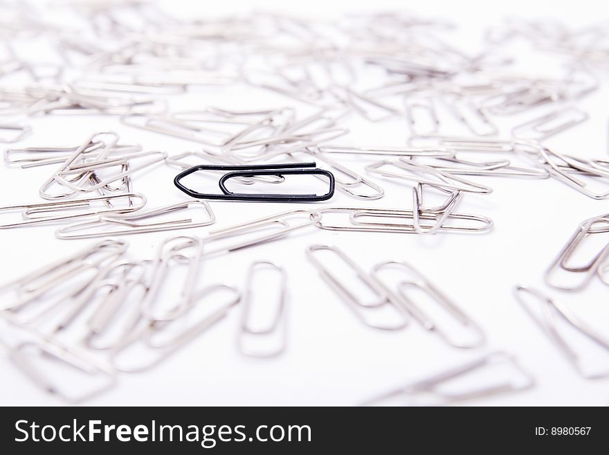 One black paperclip among many steel grey paperclips on white background. One black paperclip among many steel grey paperclips on white background