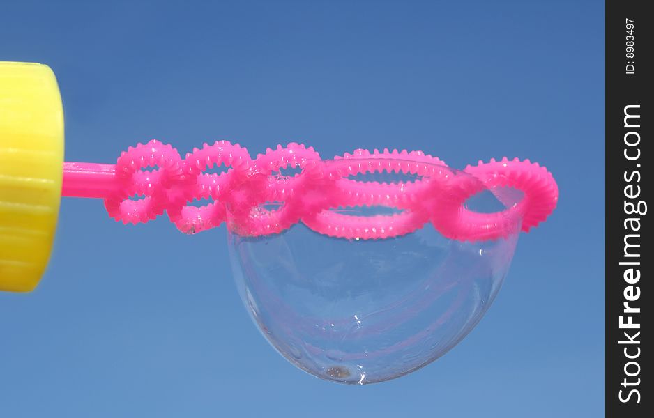 Upside down bubble on a pink wand against the bright blue sky. Upside down bubble on a pink wand against the bright blue sky