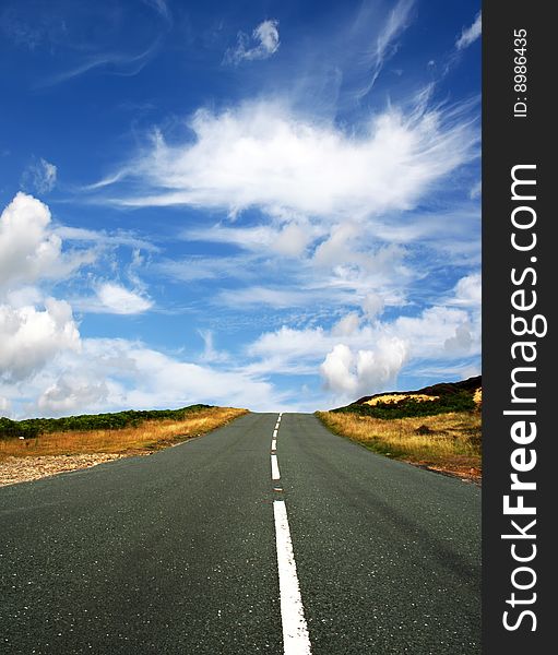 Country road leads towards blue cloudy sky