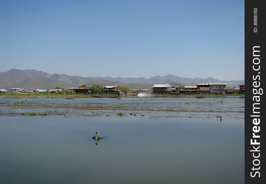 Lakeside village, mountain range and blue sky at the background. Myanmar, Burma.