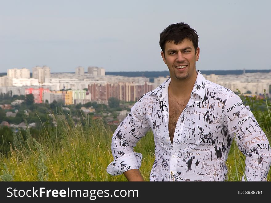 Young man in a light shirt on the grass against the backdrop of the city. Young man in a light shirt on the grass against the backdrop of the city