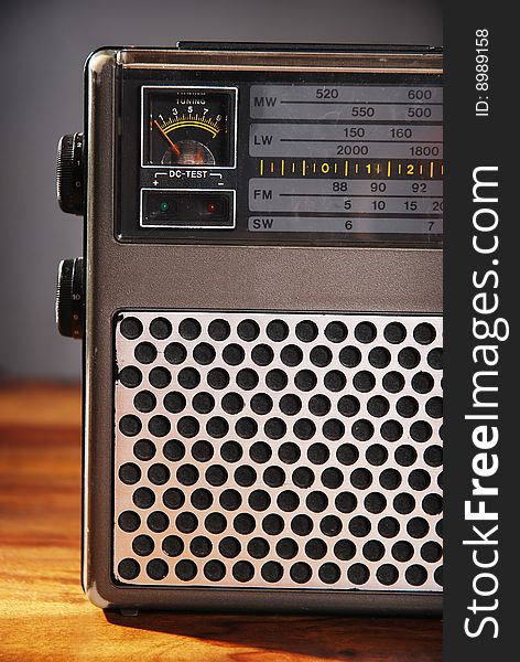 A close up view of an old fashioned radio on a wooden table in front of a dark grey background. A close up view of an old fashioned radio on a wooden table in front of a dark grey background.