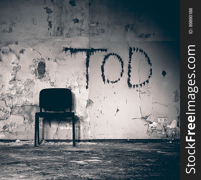 Chair leaning against wall with peeling paint and graffiti in abandoned building in black and white. Chair leaning against wall with peeling paint and graffiti in abandoned building in black and white.