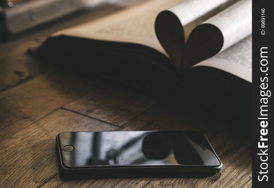 Closeup of smartphone on rustic wooden boards with open book. Closeup of smartphone on rustic wooden boards with open book.