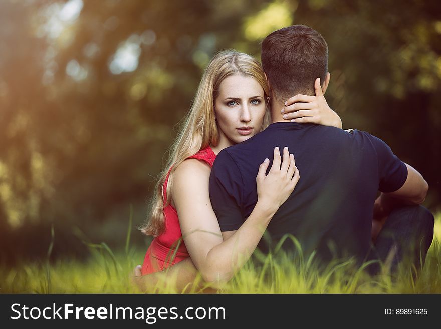 A man and a woman in a park with the woman hugging the man and looking at camera behind his back. A man and a woman in a park with the woman hugging the man and looking at camera behind his back.