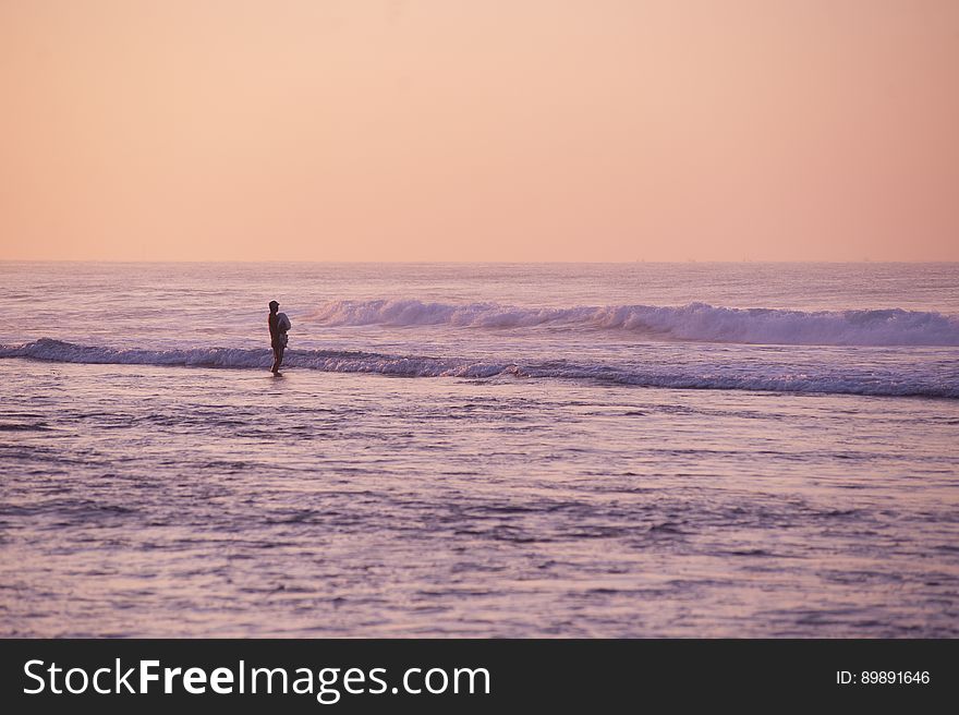 A person standing on the beach at sunset.