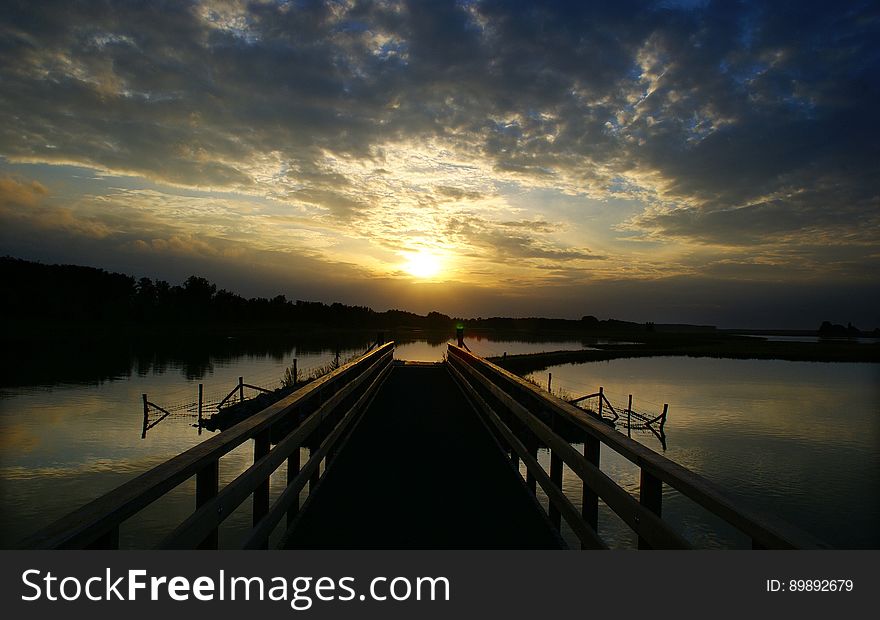 A pontoon over a lake at sunset and the silhouetted coast. A pontoon over a lake at sunset and the silhouetted coast.