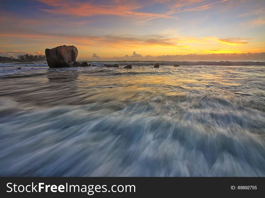 A long exposure of the waves on a beach with a rock at sunset. A long exposure of the waves on a beach with a rock at sunset.
