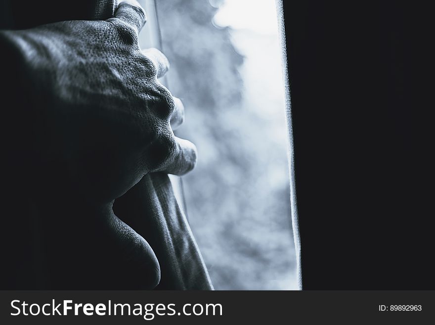 A black and white close up of a man`s hand opening a curtain. A black and white close up of a man`s hand opening a curtain.