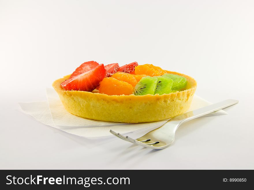 Strawberry, mandarin and kiwi custard fruit tart on a napkin with fork on a  white background. Strawberry, mandarin and kiwi custard fruit tart on a napkin with fork on a  white background