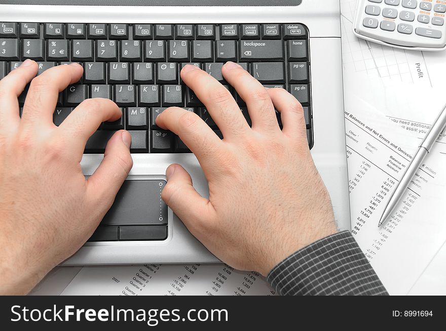 Businessman typing on notebook (laptop) on desk with scientific calculator, elegant silver pen and financial papers