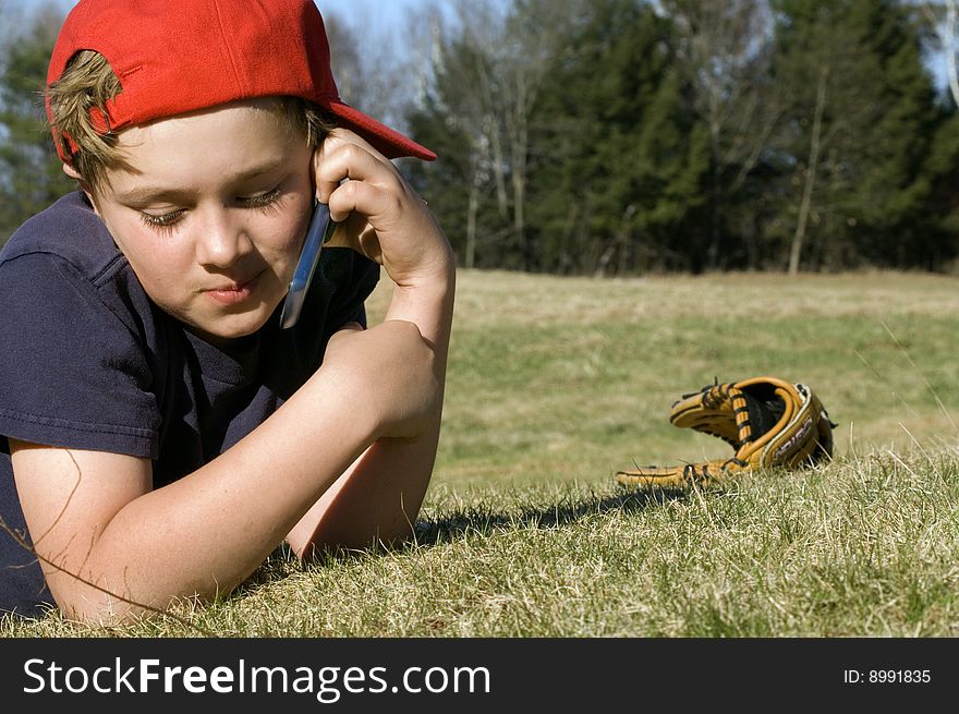 A young boy takes a break from playing baseball to chat on the cellular telephone. A young boy takes a break from playing baseball to chat on the cellular telephone