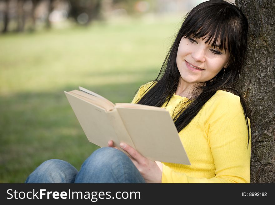Happy brunette woman reading book in park