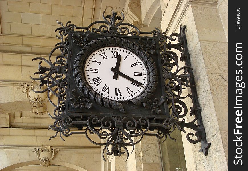 A beautiful old clock hangs in Paris on a street so people passing by can see what time it is. A beautiful old clock hangs in Paris on a street so people passing by can see what time it is