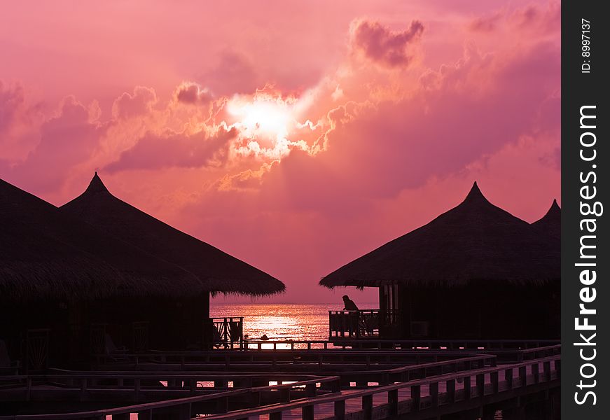 Human silhouette in water bungalow at sunset, abstract vacation background