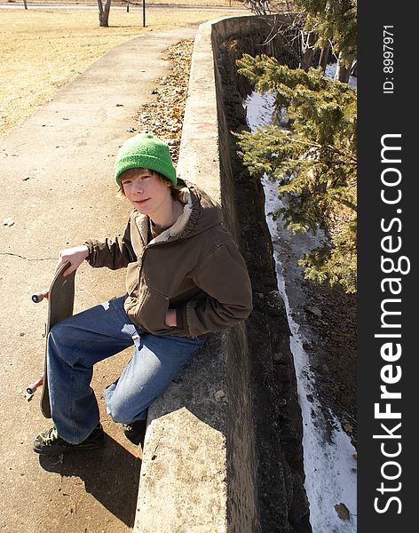 A young teen boy sits on a concrete ledge with his skateboard. A young teen boy sits on a concrete ledge with his skateboard.