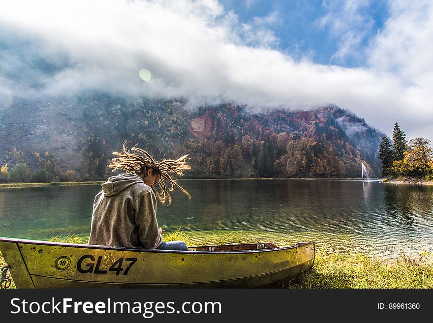Man in Brown Hoodie Sitting on Yellow Paddle Boat Beside Lake Behind Hills during Daytime