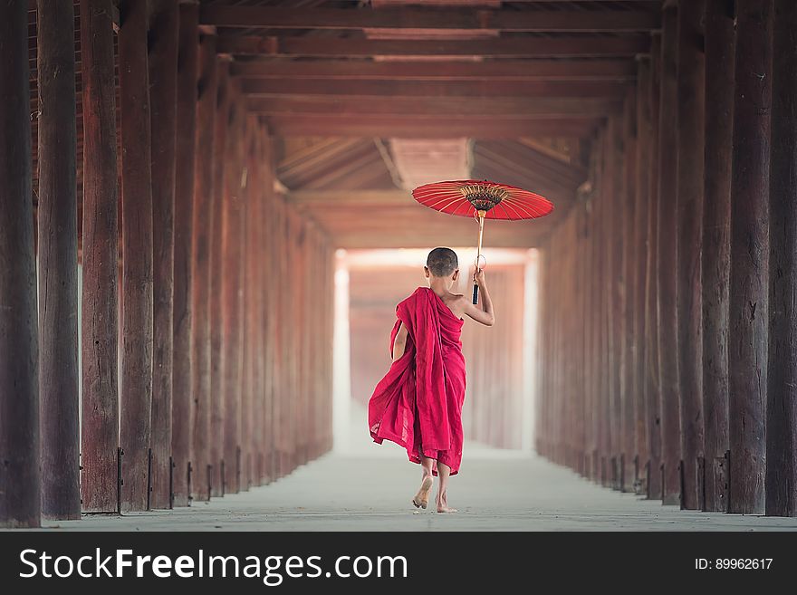 Young male monk in red robes with red umbrella walking down hallway. Young male monk in red robes with red umbrella walking down hallway.