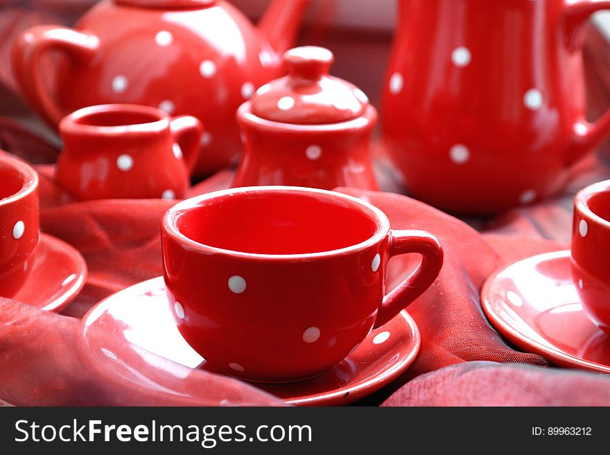 Red cups, saucers, milk jug, sugar bowl, coffee pot, all matching in red with white spots and selective focus on just one cup. Red cups, saucers, milk jug, sugar bowl, coffee pot, all matching in red with white spots and selective focus on just one cup.