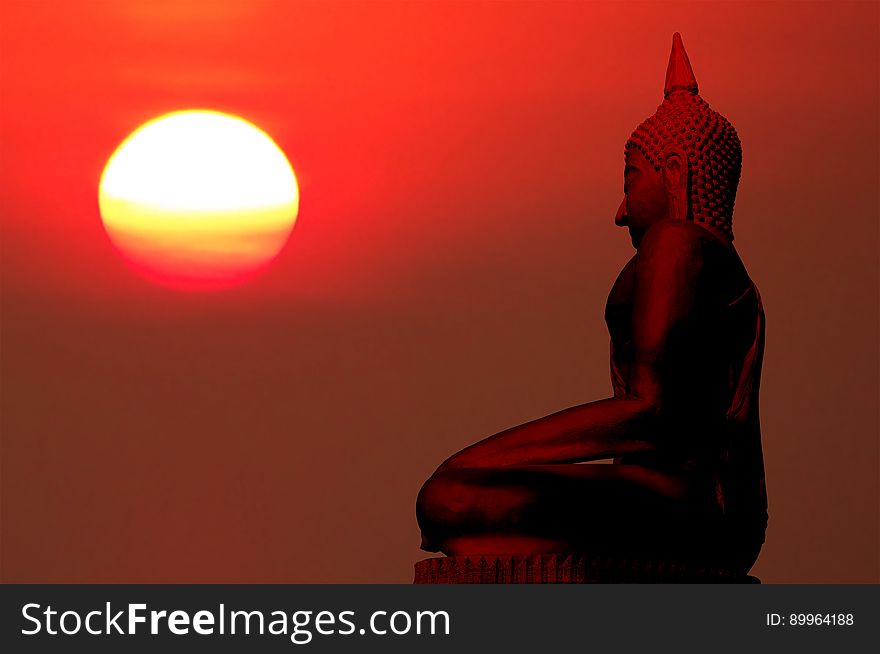 Silhouette of buddha statue with blurred sunrise background.