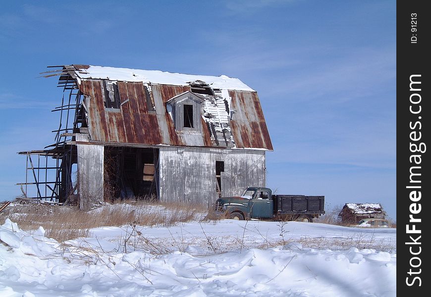 A decrepit barn and farm truck stand vigil in a wintry field. A decrepit barn and farm truck stand vigil in a wintry field.