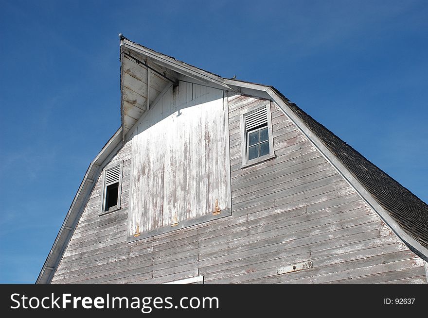 Top of a barn with worn white paint and broken windows. Top of a barn with worn white paint and broken windows