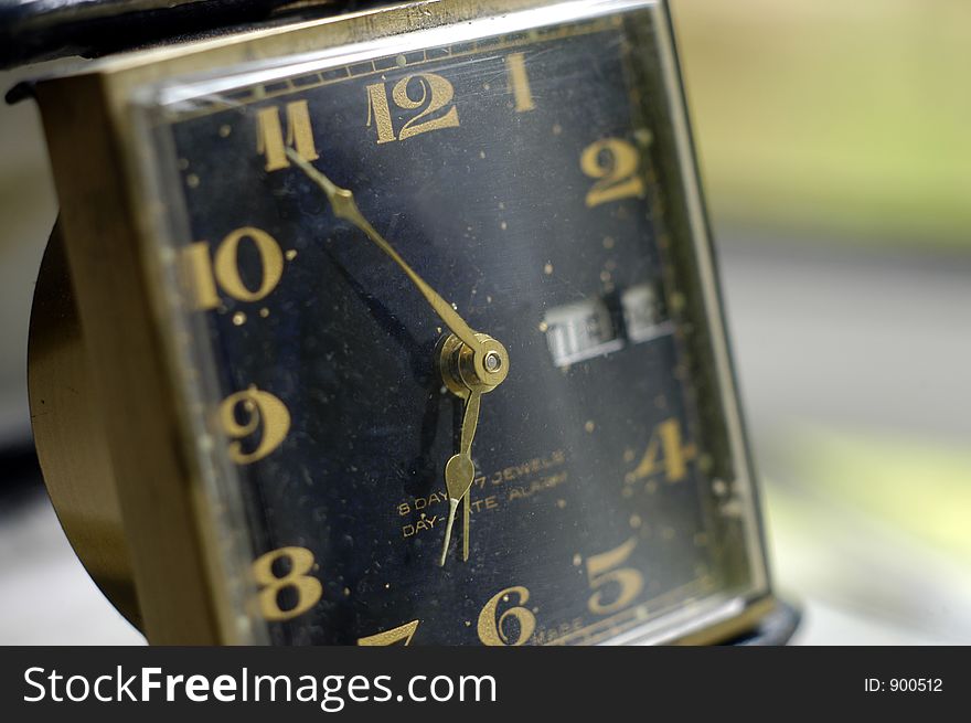 The gold hands and black face of a vintage travel alarm clock. The gold hands and black face of a vintage travel alarm clock