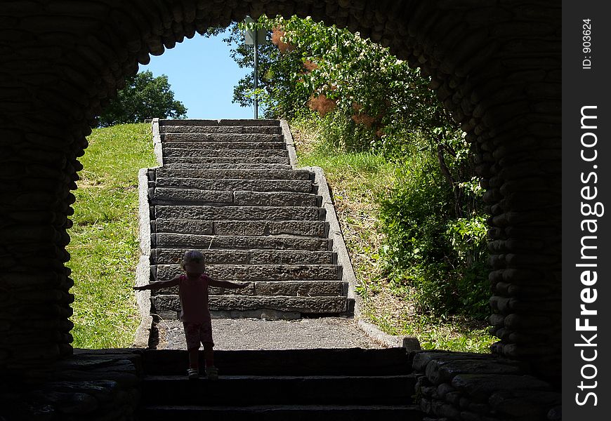 A little girl stands in the shadow of an arch with arms outstretched and stairs in the background. A little girl stands in the shadow of an arch with arms outstretched and stairs in the background.