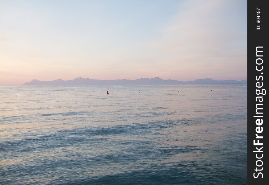 Early morning, calm sea and light red sky over mountains in background. Early morning, calm sea and light red sky over mountains in background