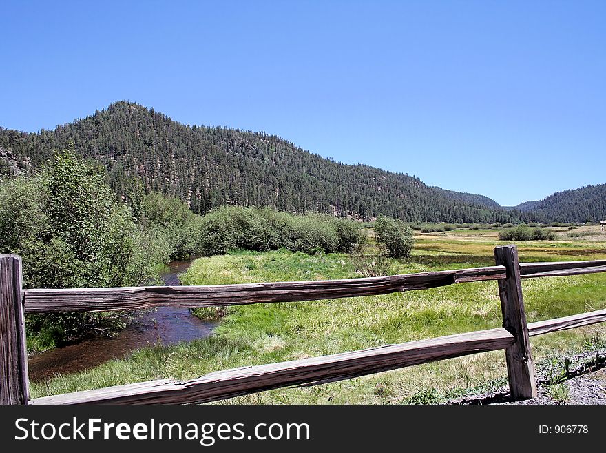 Arizona mountain stream framed by a split rail fence and blue sky