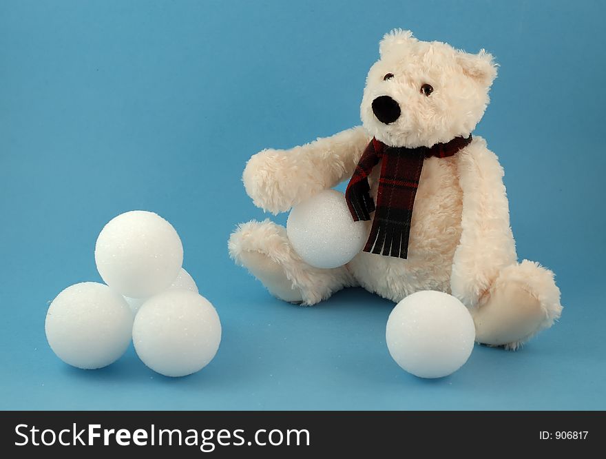 Sitting teddy bear toy with snowballs on blue background. Sitting teddy bear toy with snowballs on blue background