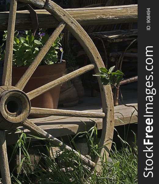 This image was taken of a wagon wheel next to a porch railing with a pot of flowers and chair in the background.