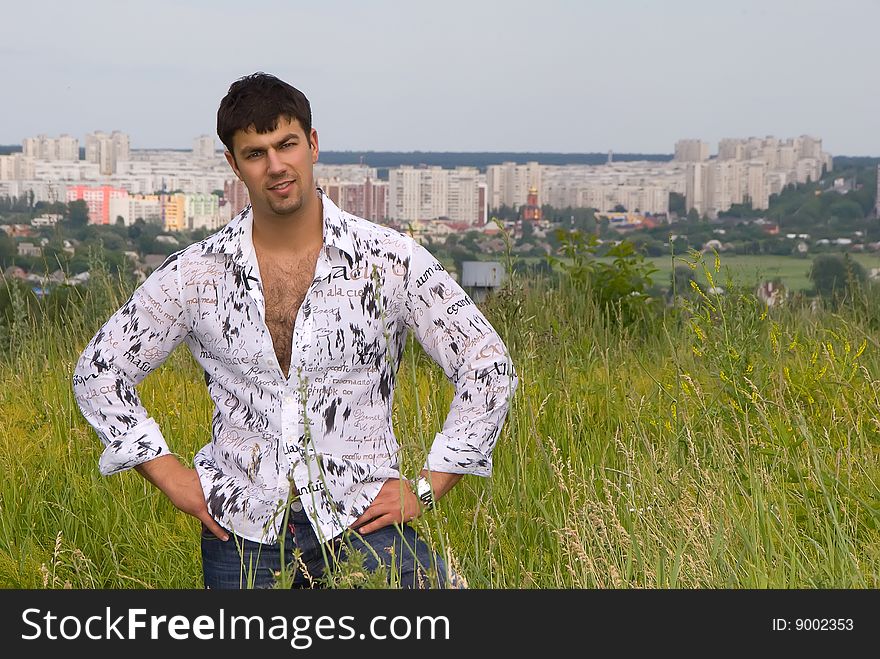 Young man in a light shirt on the grass against the backdrop of the city. Young man in a light shirt on the grass against the backdrop of the city