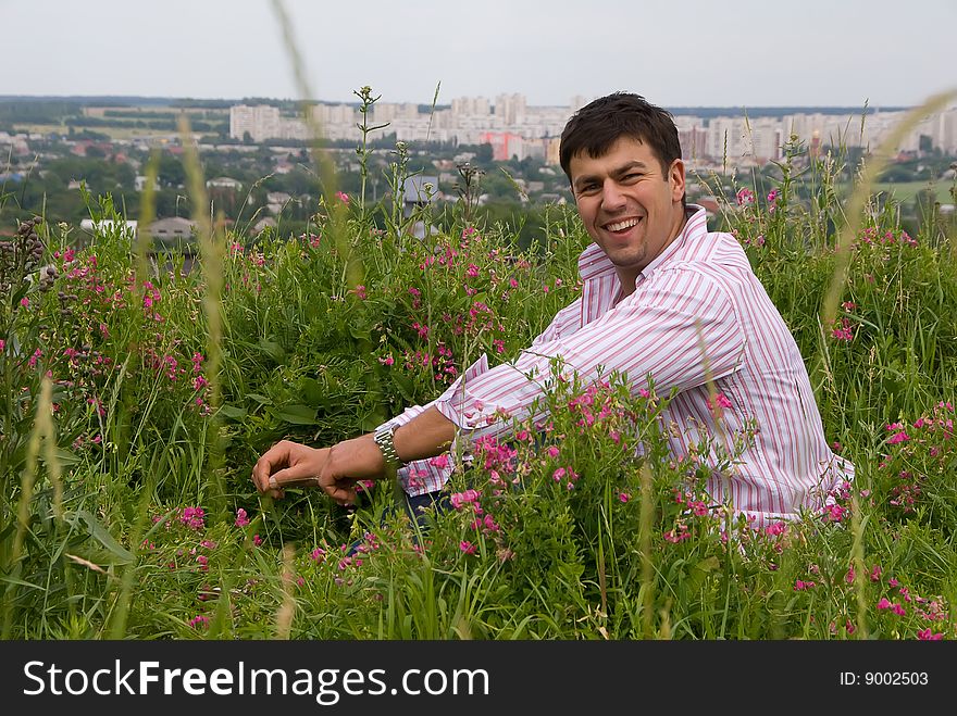 Young man in a pink shirt sitting in the flowering grass. Young man in a pink shirt sitting in the flowering grass