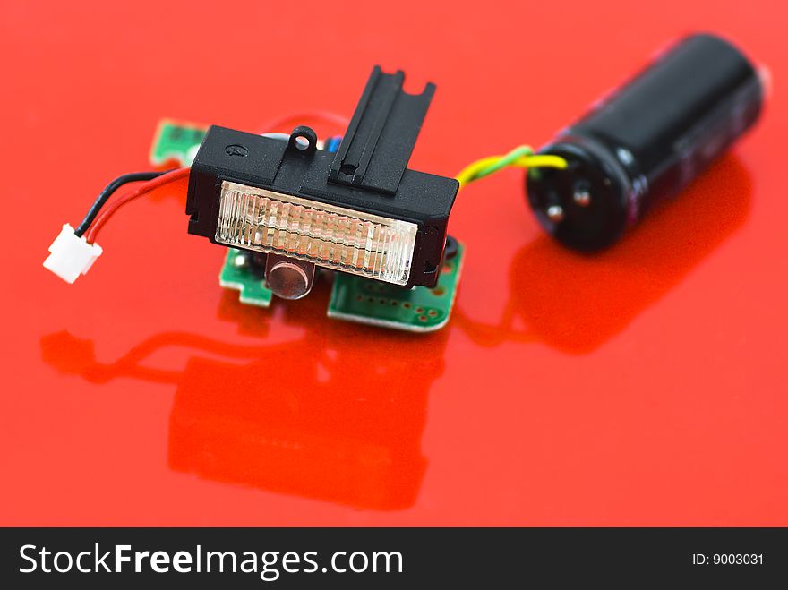 Flashlight module disassembled from compact photo camera isolated on red reflective background