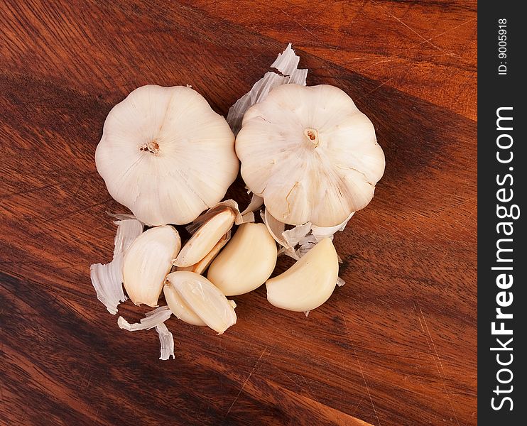 Two garlics and multiple cloves on brown cutting board. Two garlics and multiple cloves on brown cutting board.