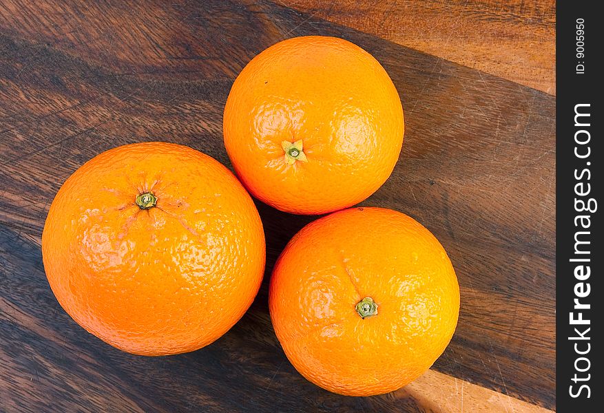 Three oranges on brown cutting board.