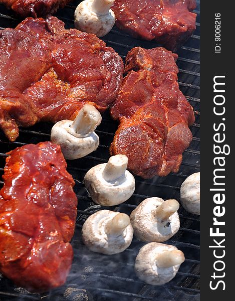 Pieces of meat and mushrooms on the barbecue.