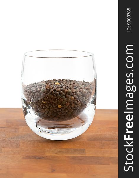 Green lentils in glass on wooden table, white background