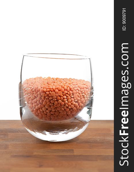 Red lentils in glass on wooden table, white background