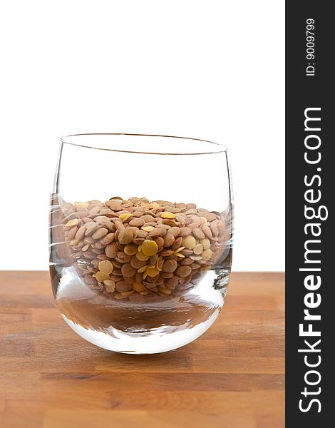 Lentils in glass on wooden table, white background