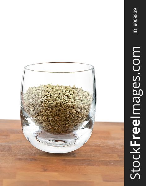 Dried fennel seeds in glass on wooden table, white background