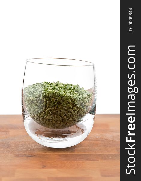 Dried chive in glass on wooden table, white background