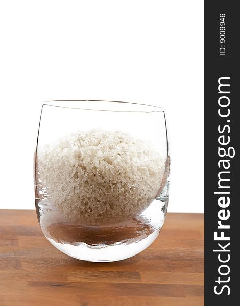 Coarse grey sea salt in glass on wooden table, white background