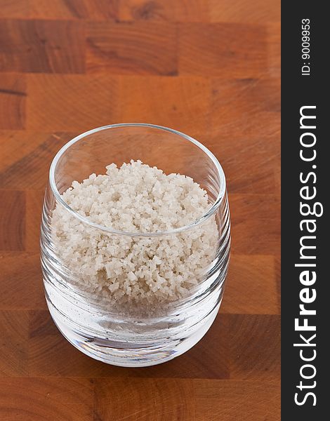 Coarse grey sea salt in glass on wooden table